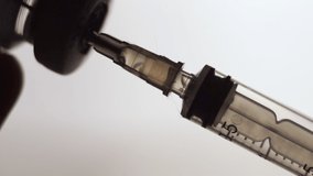vaccination concept, drawing clear liquid into a syringe close up. bubbles inside the syringein. soft grey background. horizontal slow motion macro HD video.
