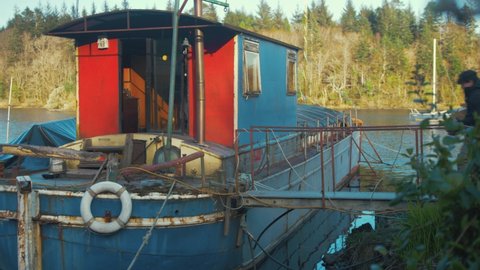 Young man living on Barge houseboat carrying logs enters wheelhouse