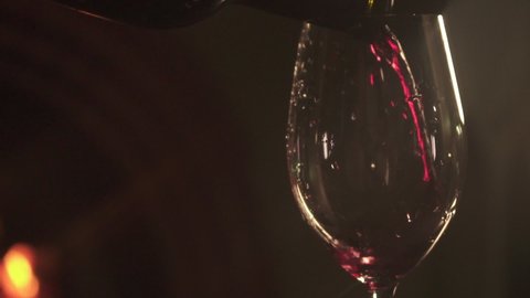 Red wine tours into the glass very slowly. A dark room with a fireplace burning in the background. 120 fps