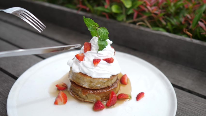 Close up of two gluten free pancakes with plant based whipped cream being cut with cutlery