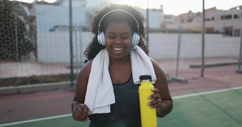 Curvy african woman smiling in camera while doing running routine in the city - Plus size and sport workout concept