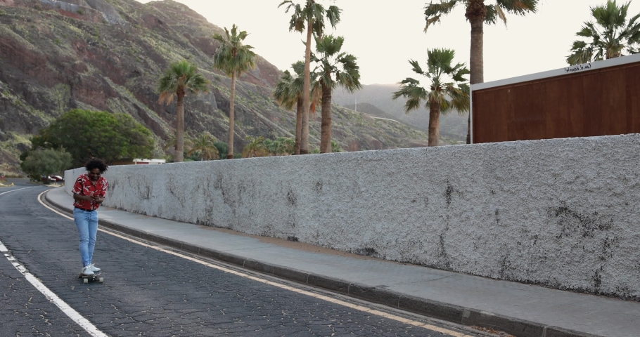 African american man riding a longboard on the road with palm trees in the background