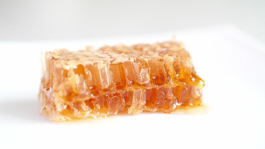 The honeycomb is cut with a knife on a white plate and honey flows out.