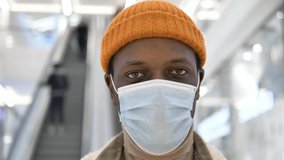 Close-up portrait of African-American man wearing a medical coronavirus protective mask and an orange hat, looking earnestly at the camera in a shopping mall - Powered by Shutterstock - Get 15% off with code: PIKWIZARD15