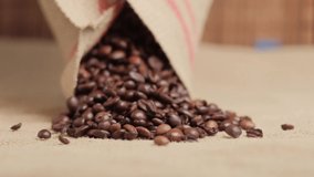 Close-up of roasted coffee beans spilling out of a burlap sack. An ingredient for making coffee. Environmental materials. Natural coffee. 4k video.