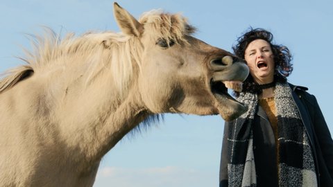 Young woman yawning together with Konik Polski horse against clear blue sky