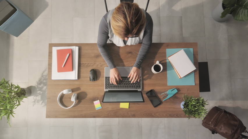 overhead top down view of woman using laptop computer at her desk,caucasian female businesswoman typing at the notebook drinks coffee shot from above Royalty-Free Stock Footage #1072573220