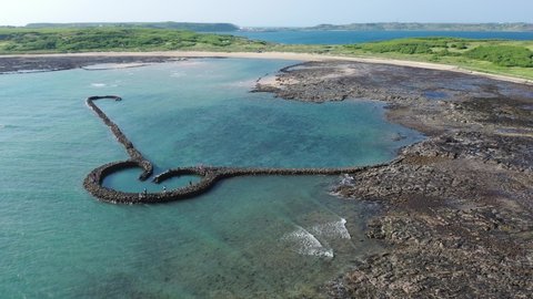 Aerial view of the One-Heart Stacked Stones (Eye of Tiger Fish Trap) bathed in the turquoise sea water, which is a traditional fishing weir and a popular tourist attraction, in Xiyu, Penghu, Taiwan