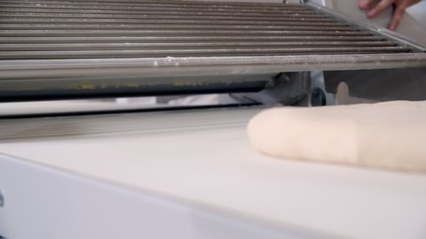 Close-up of piece of dough on the bakery dough rolling machine. Slow motion