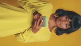 Vertical video of shocked dark skinned young woman feels surprised looks with disbelief at camera points at smartphone display fascinated by exciting news or received comments on her blog post.