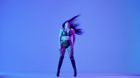 Sexy brunette in black leather lingerie is dancing erotically in a dark studio illuminated by blue lights. Sensual stripper dance, private dance, go go. Slow motion.