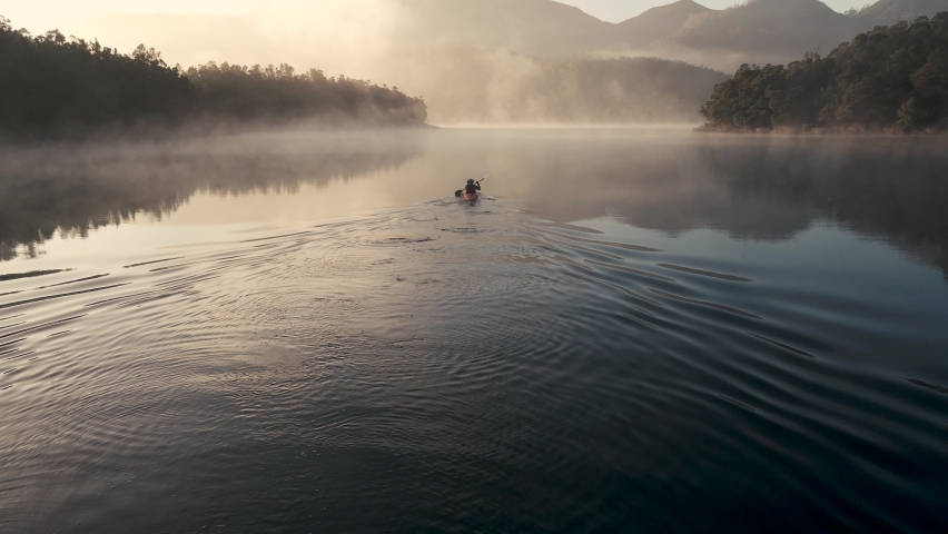 4K Drone footage of young indian kayaking in misty lake surrounded with mountains during sunrise in Ooty, Tamil Nadu, India 60FPS for slow motion