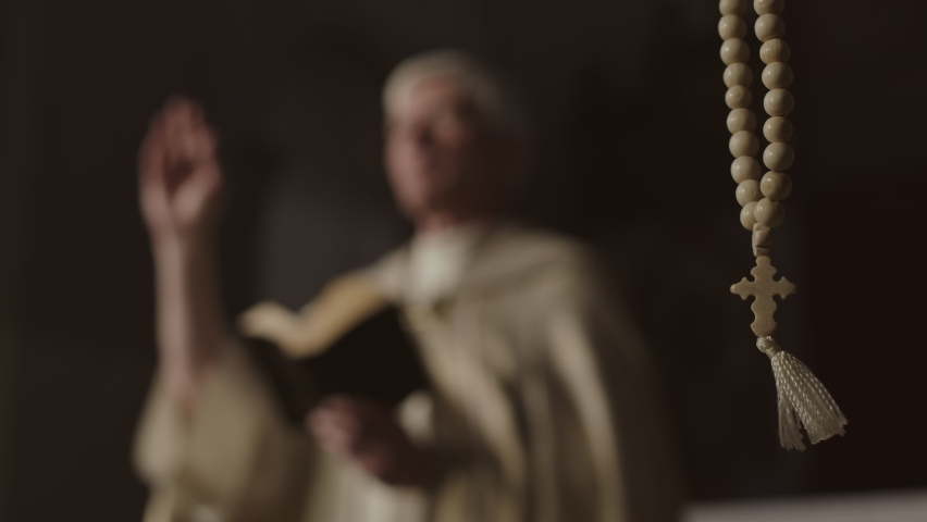 Close up of rosary beads hanging in Christian church and unrecognizable elderly priest wearing festive golden robe preaching on background Royalty-Free Stock Footage #1072586126