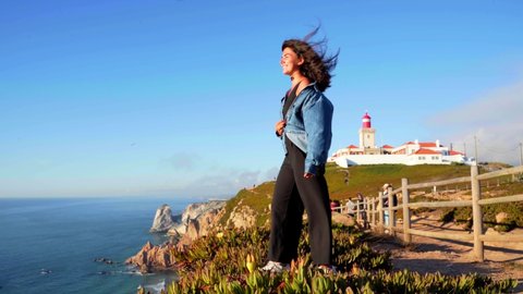 A girl stands on the edge of a cliff enjoying the view at the lighthouse at Cabo da Roca in Sintra, Portugal.