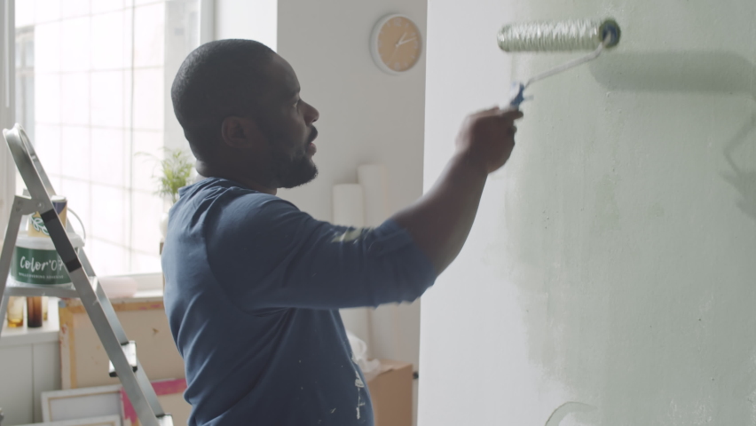 African American man painting wall in green color with roller cover while renovating room in apartment Royalty-Free Stock Footage #1072590095