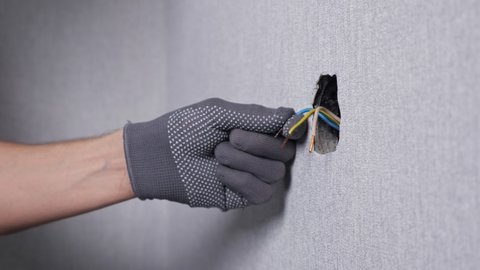 Professional electrician in gloves inserts coloured wires into socket support and screws with screwdriver at new apartment wall close view