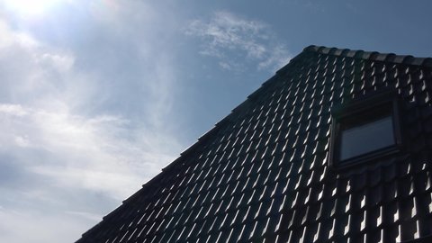 Time lapse of a roof window in velux style with black roof tiles - clouds passing by in a blue sky