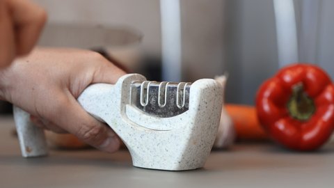 Manual sharpening of a knife in a special sharpener in a kitchen. Man hands with knife in close-up