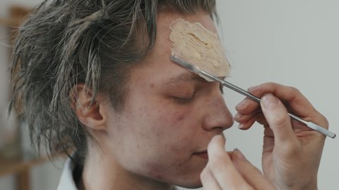 Close up shot of unrecognizable female SFX makeup artist putting prosthetic piece on forehead of male actor