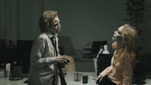 Medium shot with slowmo of zombie man with SFX makeup and torn dirty clothes giving gift to zombie girlfriend in office