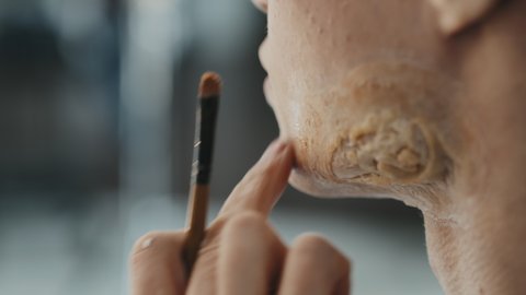 Close up shot of unrecognizable SFX artist applying makeup on prosthetic scar on face of male actor