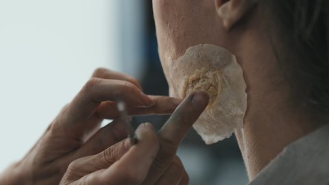 Close up shot of unrecognizable female SFX makeup artist applying prosthetic scar on face of male actor