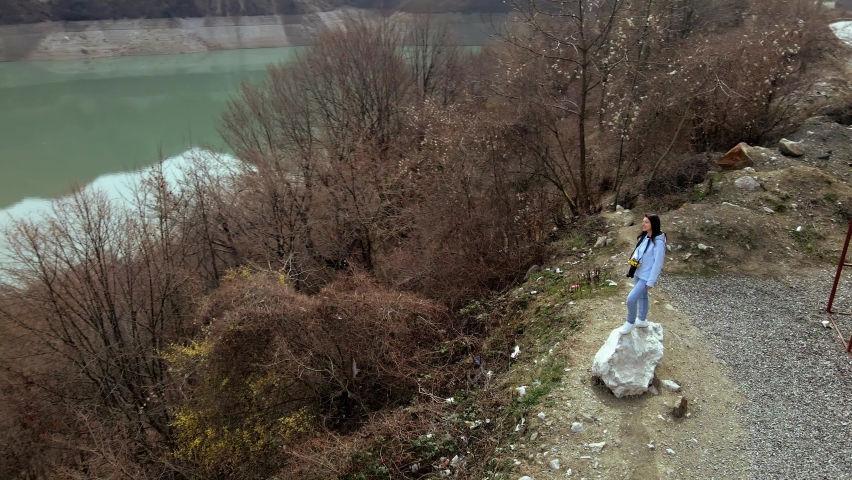 A young girl with a camera enjoys the incredible natural landscape while standing on the edge of a hill overlooking the Zhinvali reservoir