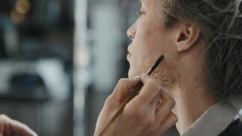 Close up of hands of unrecognizable MUA applying SFX makeup around prosthetic scar on face of male actor