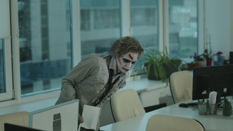 Tracking shot of zombie businessman in dirty and torn shirt with necktie and SFX makeup with fake wound holding documents and walking in office
