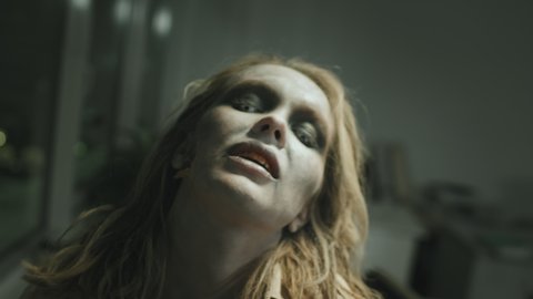 Close up tracking shot of angry zombie woman with SFX makeup and stained teeth grunting and walking towards camera
