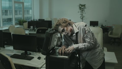 Medium shot of zombie businessman with SFX makeup and torn dirty shirt and necktie using copier in office