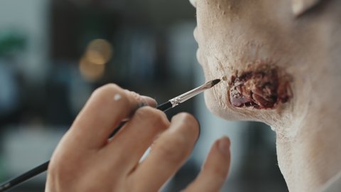 Close up shot of unrecognizable SFX artist using brush and creating fake wound on chin of male model
