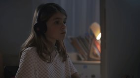 Portrait of a girl in headphones without a brand listening to music in front of a computer. Teenager dances shaking his head in front of the screen. Livestyle video of a teenager at home.