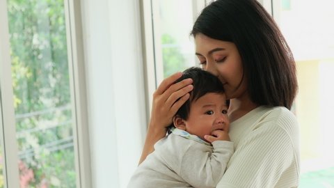 Happy young asian mom holding cute adorable infant child in livingroom. Cheerful adult mother lull a kid baby having love together in home. Parents and daughter activity and Health care concept.
