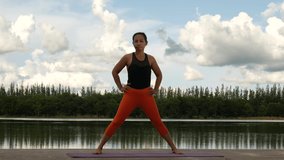 A woman practicing yoga by the water in the evening