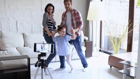Happy young family dancing at home with his little cute daugther, shooting video.