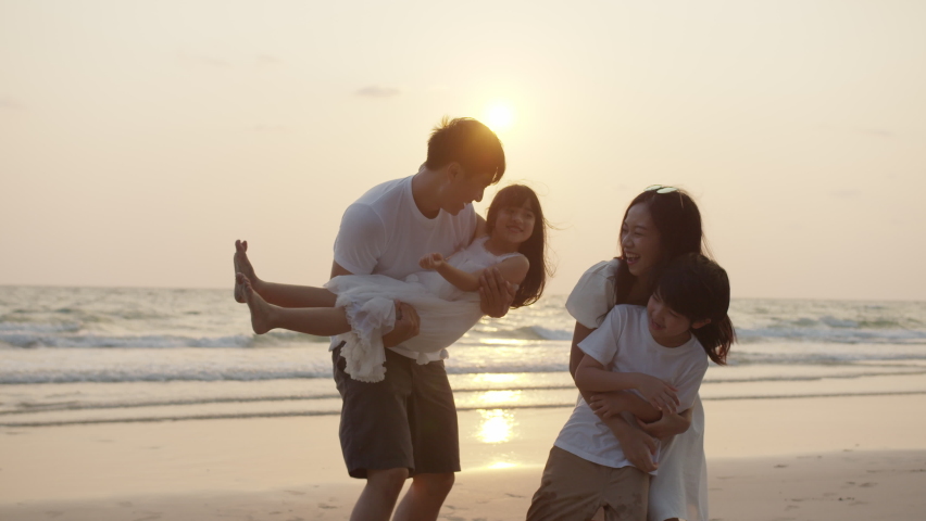 Silhouetted happy asian family playing and having fun on the beach at sunset. Freedom, Relationship, embrace and Travel concept. Positive emotion and feeling warmwith sun flare in evening. | Shutterstock HD Video #1072613804