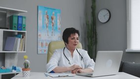 Medical female doctor wears white coat, video calling distant patient on laptop. Doctor talking to client using virtual chat computer app. Telemedicine, remote healthcare services concept