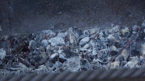 Smouldering embers close-up. From them comes a small smoke and flies ash. A slight red flicker is visible