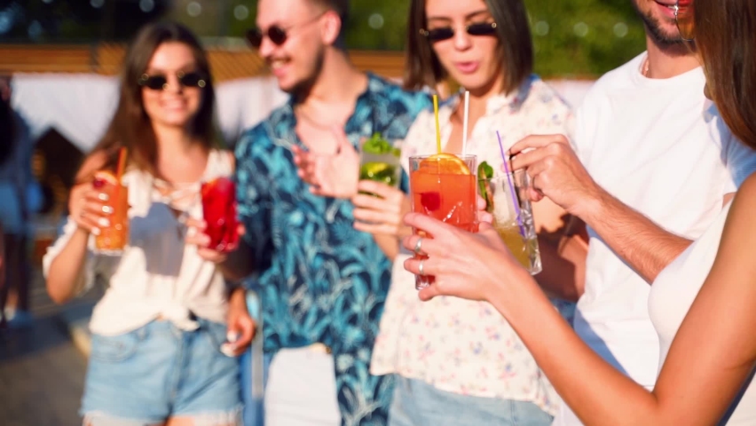 Close view of friends having fun at summer pool party, clinking glasses with cocktails and dancing near hotel swimming pool outdoors. People toast drinking juice at luxury villa in slow motion. Royalty-Free Stock Footage #1072623710