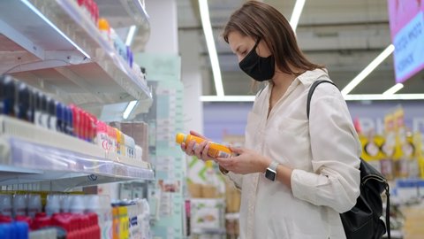 Young woman comparing two spray antiperspirants in the store trying to choose the better one. COVID-19 restrictions require to wear masks