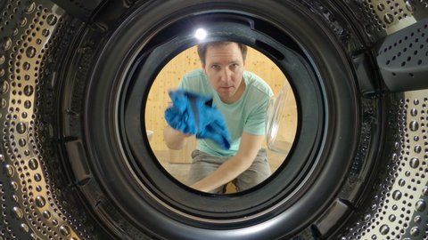 SLOW MOTION, CLOSE UP, PORTRAIT: Man loads up the washer with lingerie, briefs and other clothing while doing chores. Young male is loading up the washing machine with dirty laundry while housekeeping