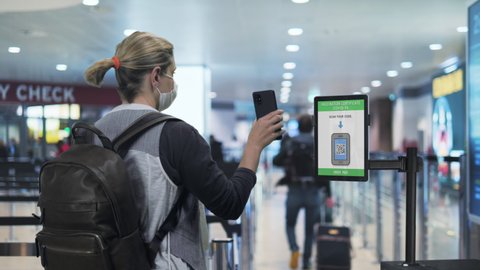 Covid-19 travel safety measures,young tourist woman showing health passport green card at the airport security control,female traveller scans digitale vaccination certificate