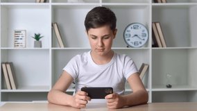 Beautiful boy 13 years old playing mobile game on smartphone at home. Teenager playing mobile phone. Kid using phone for gaming. Child playing video game indoors