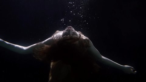 slowed down underwater portrait of woman facing the light floats up unconscious