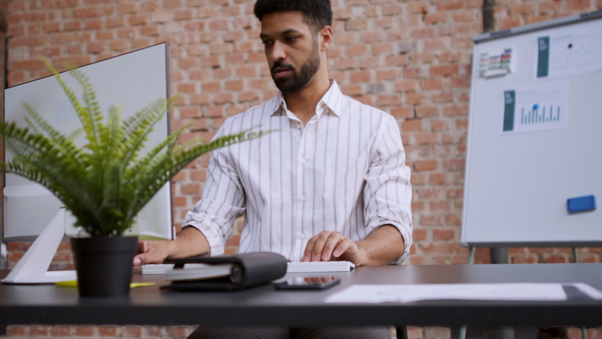 Young businessman in office working on pc and looking at camera.