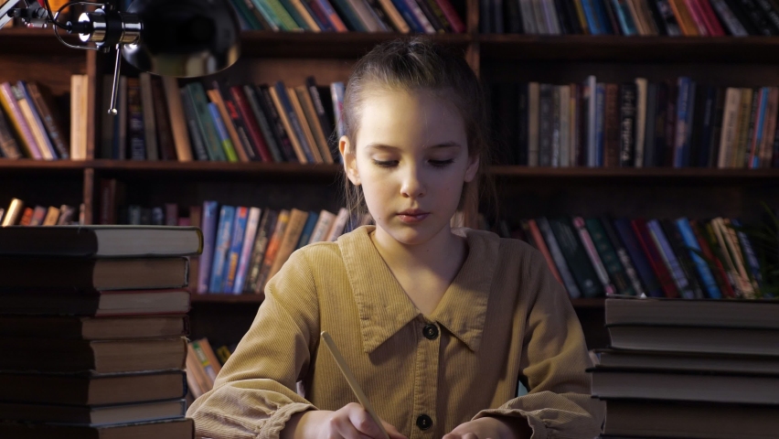 Exhausted young lady writes home assignment in copybook with brown pencil sitting among different books at home in late evening closeup