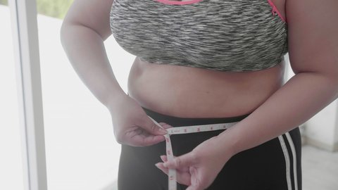 Woman fat in sportswear measuring waist with tape for control weight at home, plus size, female with overweight and obesity dieting with weight loss, health care and body care with workout.