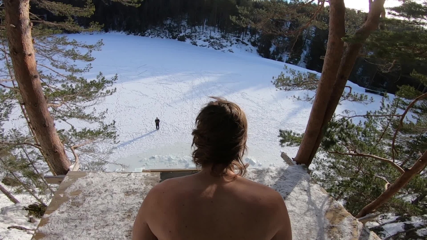 Crazy man takes a dangerous cliff dive into a hole cut in the ice of a lake far below Royalty-Free Stock Footage #1072642871