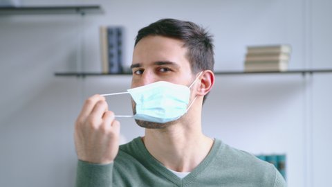 Young attractive male taking off a blue medical mask. Young man smiling when taking off mask